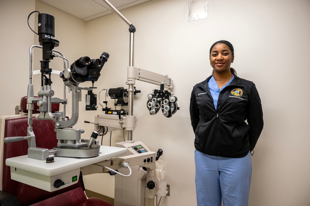 A woman stands beside equipment used by eye doctors.
