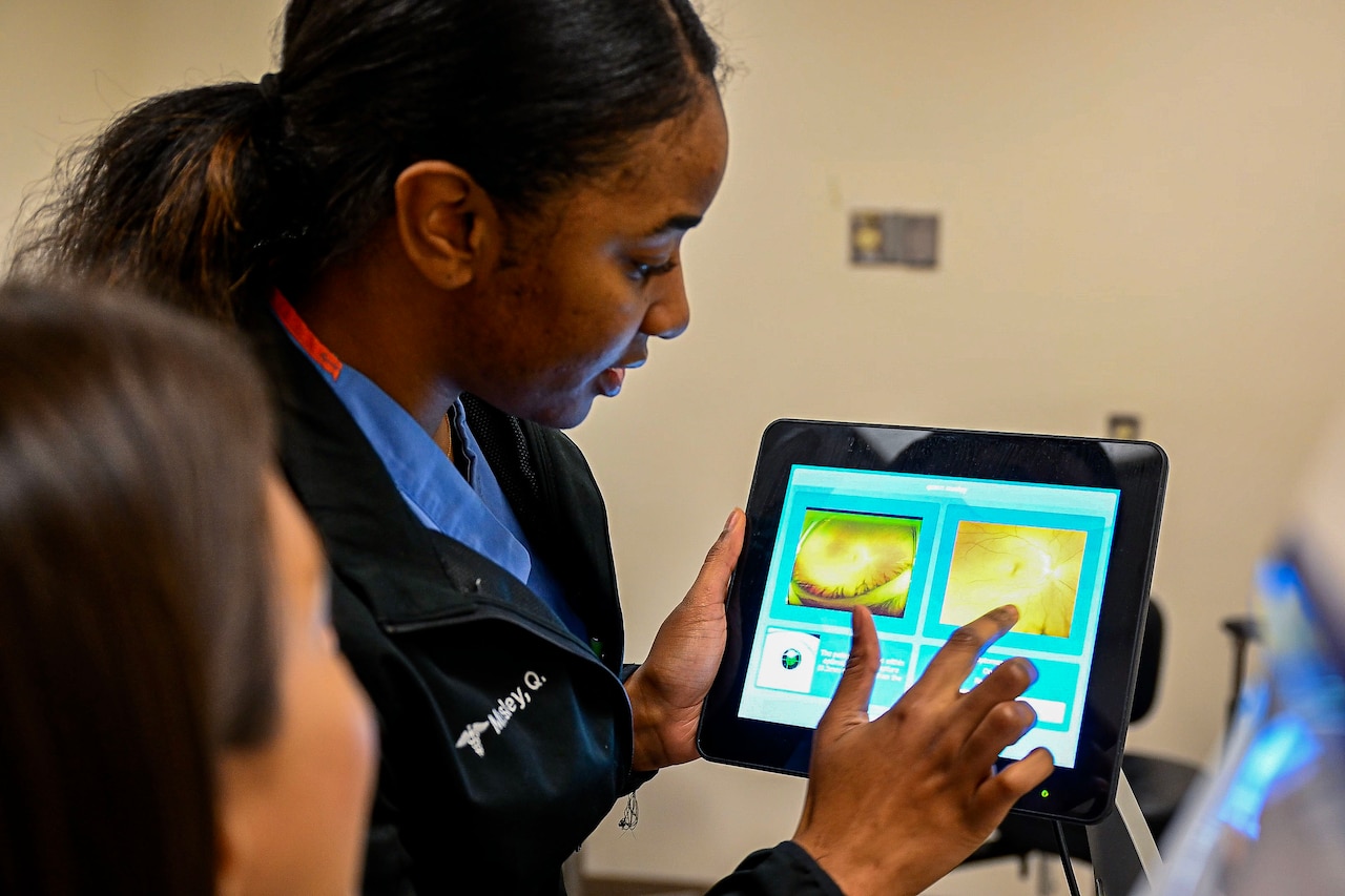 A woman points to an image on a tablet while a patient looks on.