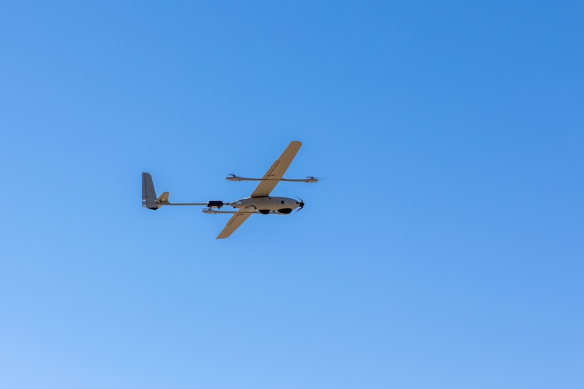 A long drone with wings flies in a blue sky.