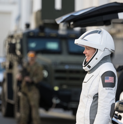 A woman astronaut, suited up, looks left.