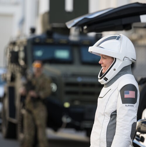 A woman astronaut, suited up, looks left.
