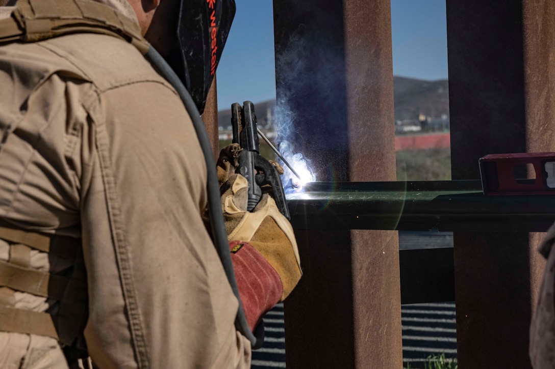 A marine wearing protective face gear welds a metal bar onto metal posts.