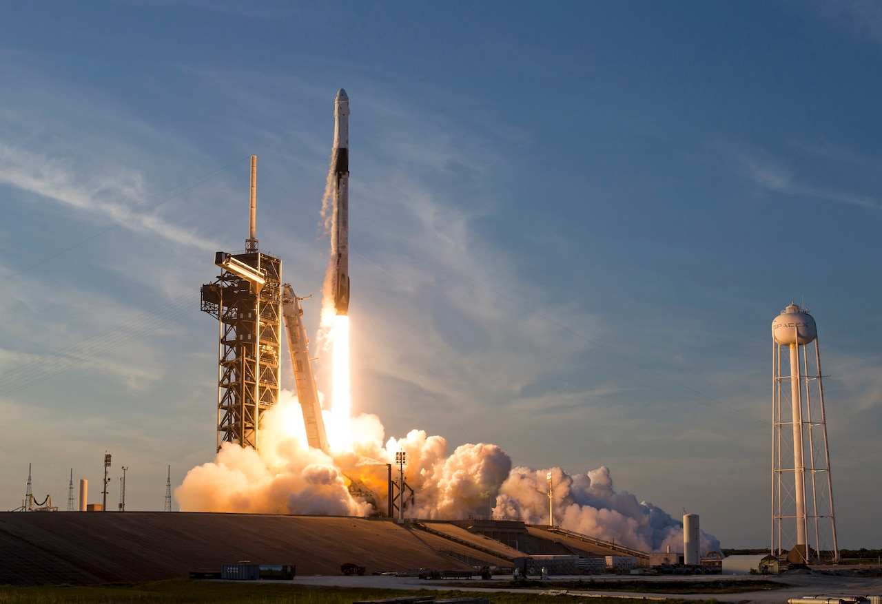 A rocket launches into a blue sky and leaves fiery smoke behind.