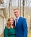 Husband and wife pose together in formal clothing outside their home