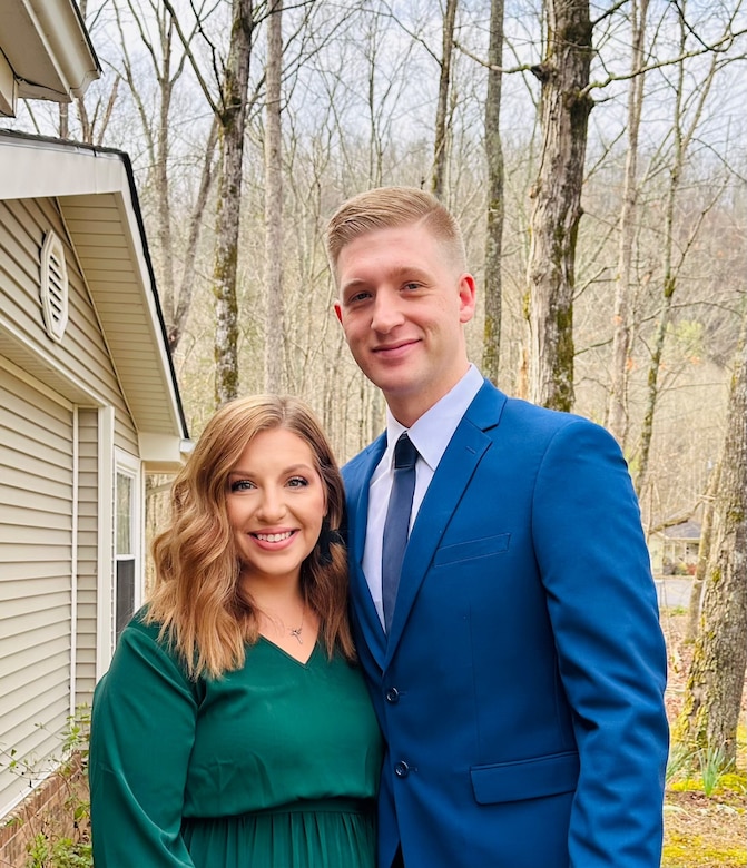 Husband and wife pose together in formal clothing outside their home