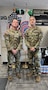 2 male U.S. Army Soldiers in uniform pose together in an office space in front of the American Flag and USAREC Flag