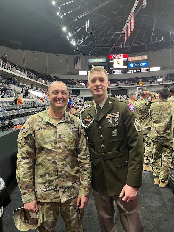 Male U.S. Army Soldier in AGSU poses with male U.S. Army Soldier in ACU on the court of a basketball stadium