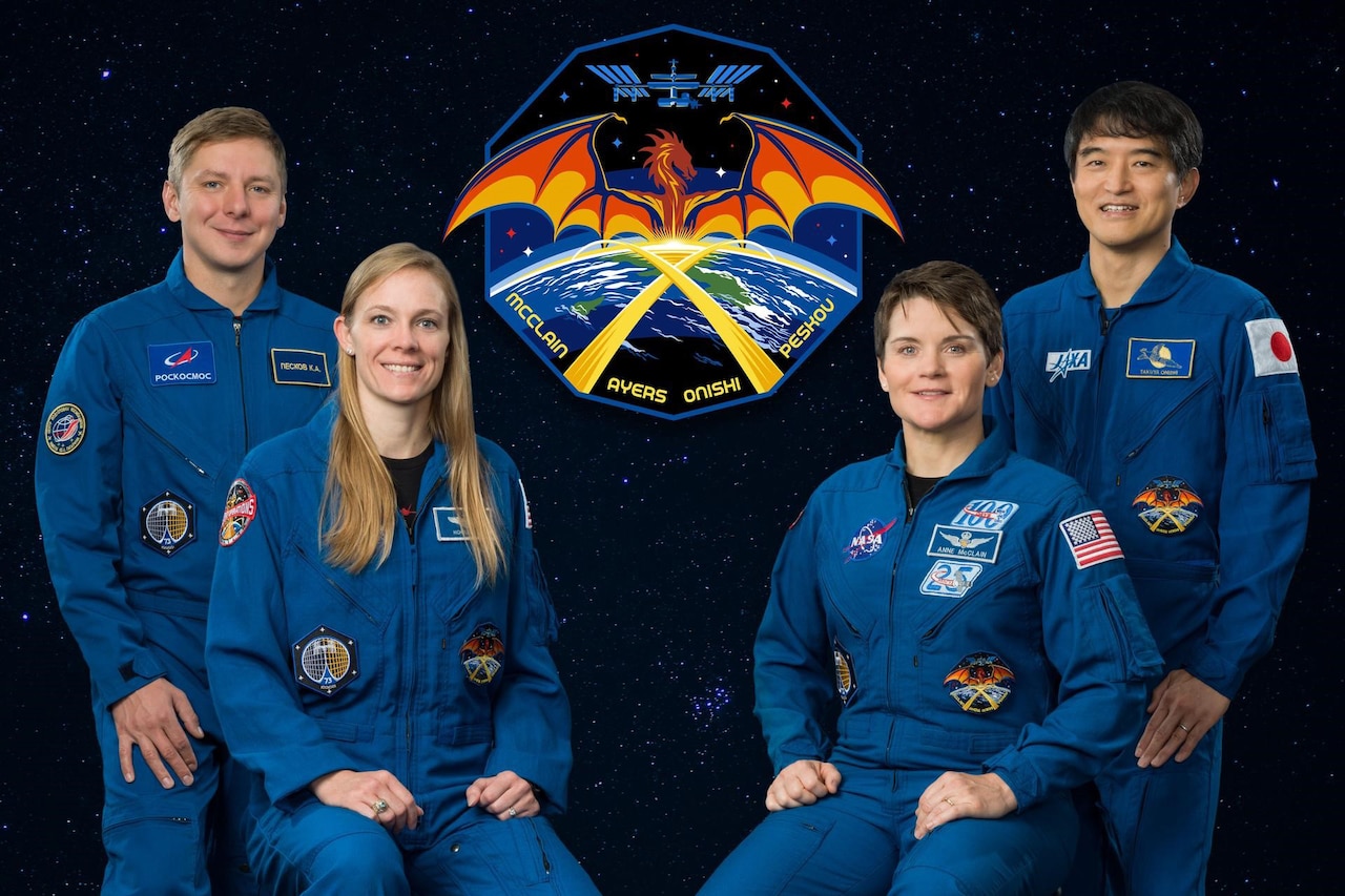 Four astronauts pose in front of a starry background with a logo of a dragon over Earth and a satellite.
