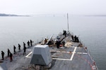 People wearing military uniforms line the edge of ship as it heads out to sea.
