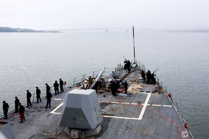 People wearing military uniforms line the edge of ship as it heads out to sea.