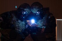 Two Airmen in MOPP gear read a field manual