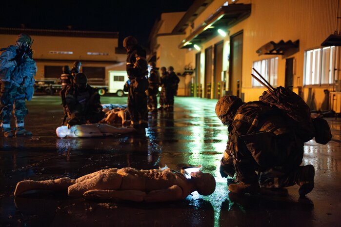 Airmen in MOPP gear surrounding practice dummies on ground