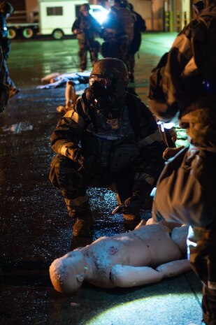 Airman in MOPP gear kneeling next to practice dummy on ground