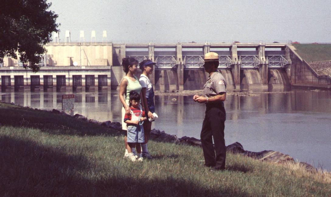 Vintage picture of a park ranger talking to a family in front of a dam.