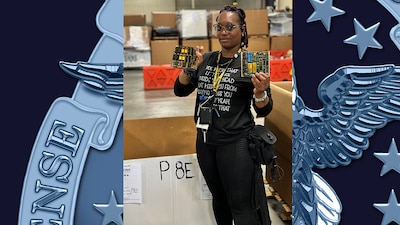 A woman in a warehouse holds up circuit boards.