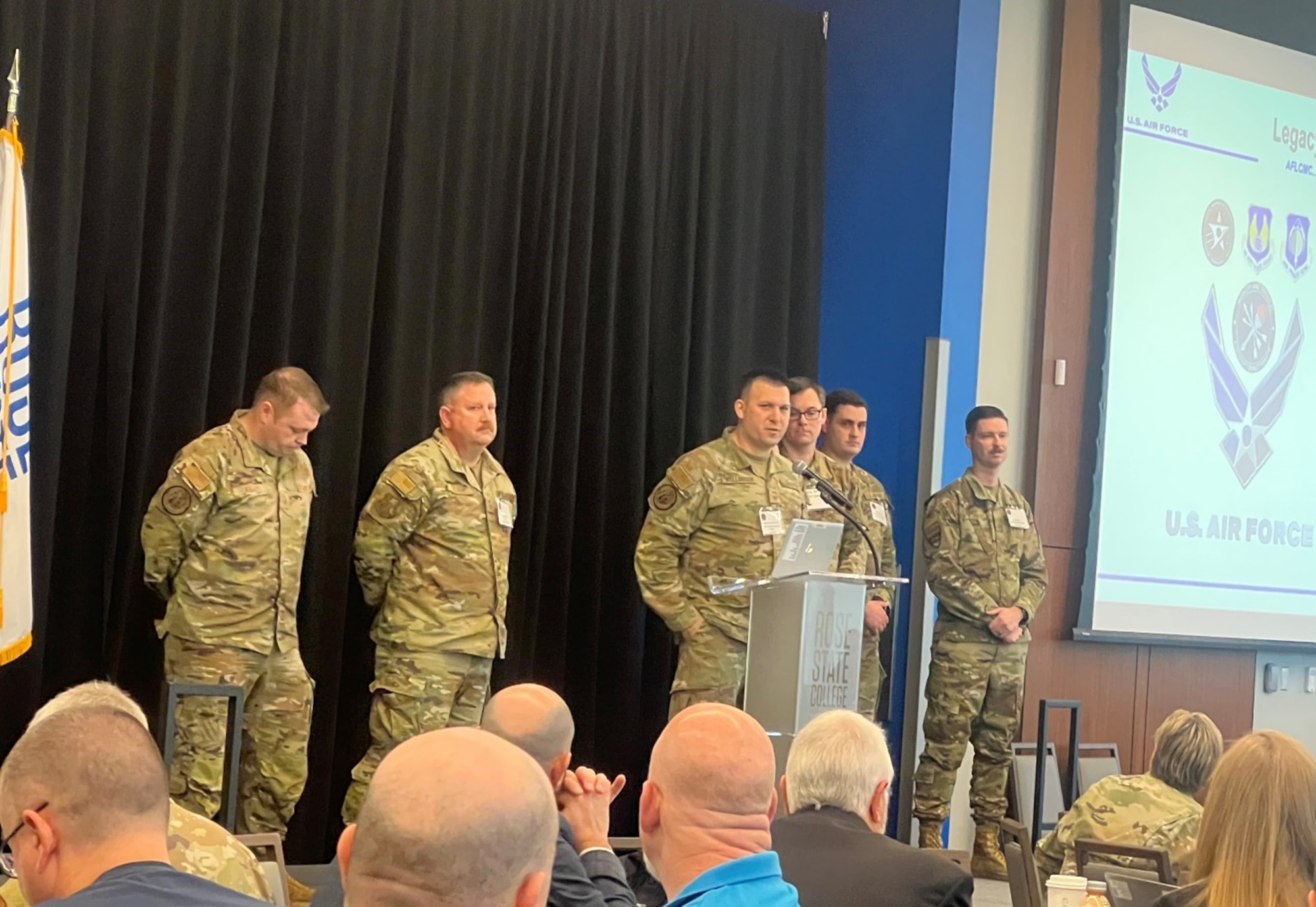 Men in Air Force OCPs talking on stage.