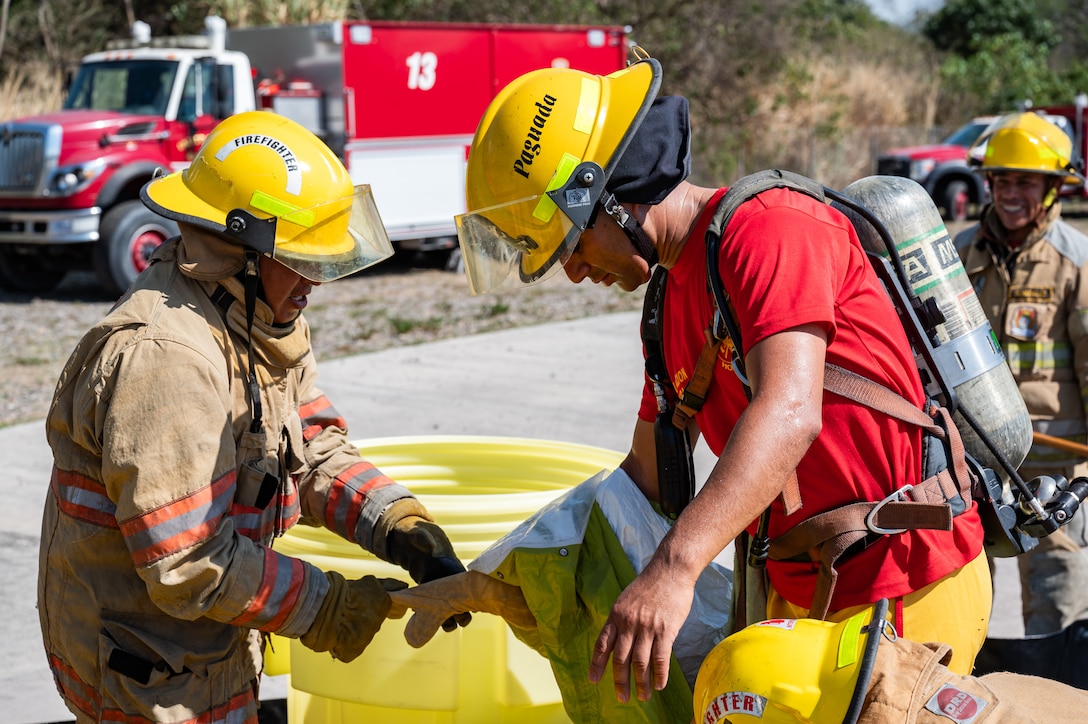 A local Honduran firefighter assists in removing hazmat gear from a Joint Task Force-Bravo firefighter during a hazmat exercise at Soto Cano Air Base, Honduras, March 14, 2025.