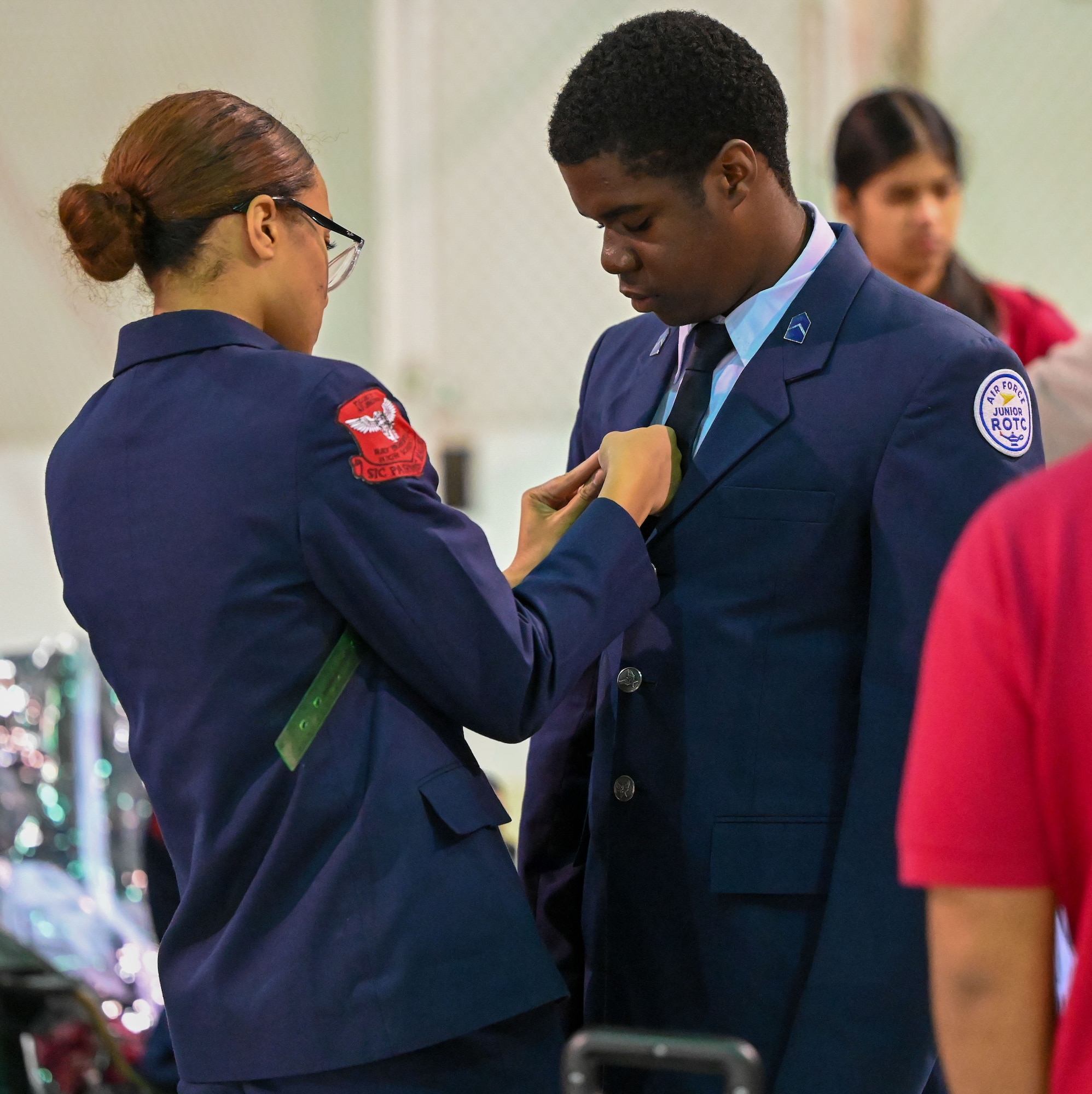 A Junior Reserve Officers' Training Corps (JROTC) cadet assists a teammate with a uniform adjustment before competition at the JROTC Drill Competition at Tinker Air Force Base, Oklahoma, Feb. 15, 2024. The event, held on base for the first time in more than 20 years, emphasized precision, discipline, and teamwork. (U.S. Air Force photo by Garrett N. Cole)