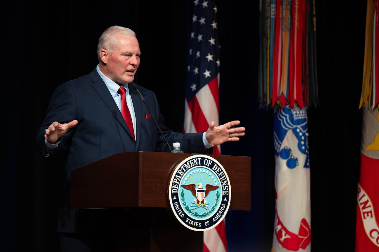 A man in a suit and tie speaks at a podium behind a lectern.