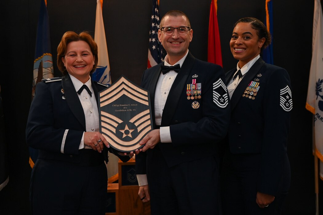 U.S. Air Force Col. Angelina Maguinness, 17th Training Wing commander, left, Chief Master Sgt. Khamillia Washington, 17th TRW command chief, right, present Chief Master Sgt. Brandon Abbott, 17th Training Group senior enlisted leader, middle, with his plaque at the 2025 Chief Master Sergeant Recognition Ceremony in the Powell Event Center at Goodfellow Air Force Base, Texas, March 14, 2025. Abbott is the principal advisor to the 17th TRG commander on all matters influencing joint and international military training. (U.S. Air Force photo by Senior Airman Evelyn J. D’Errico)