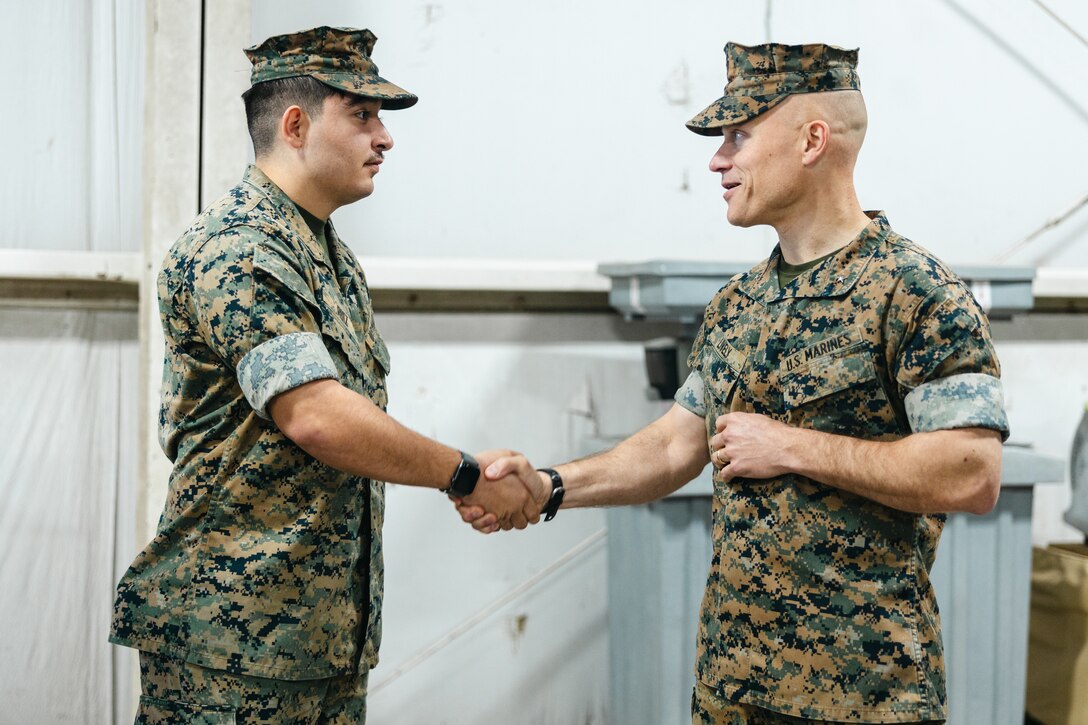 U.S. Marine Corps Lance Cpl. Jesus Ruiz, left, a food service specialist with 3d Battalion, 2d Marine Regiment, 2d Marine Division, is presented a challenge coin by Brig. Gen. James W. Lively, the assistant division commander of 2d MARDIV, for his support during operations across the Division on Marine Corps Base Camp Lejeune, Jacksonville, North Carolina, March 14, 2025. Food service Marines support the operational requirements of 2d MARDIV by providing Marines with meals throughout their deployments and training environments. (U.S. Marine Corps photo by Lance Cpl. Frank Sepulveda Torres)