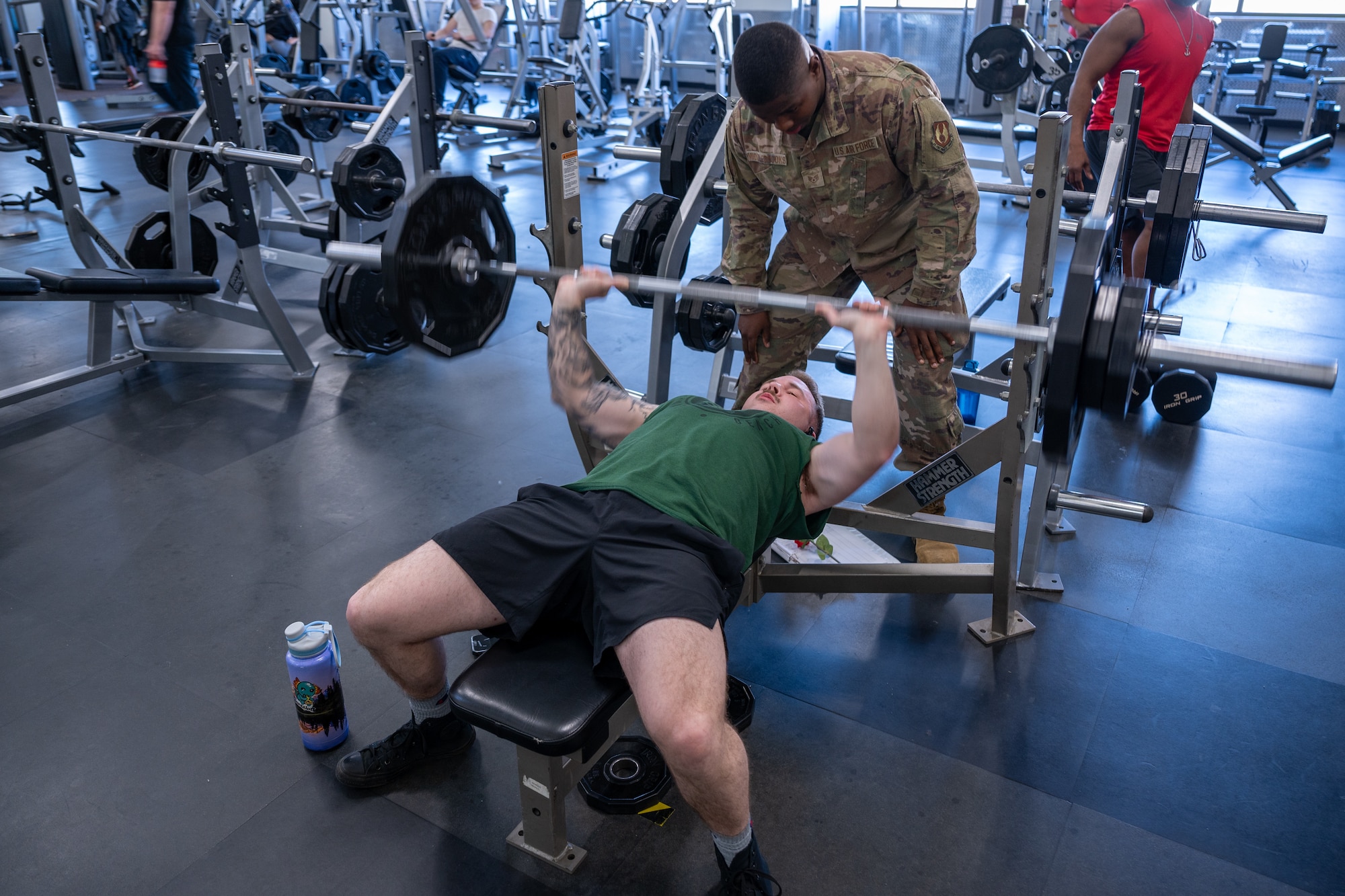 Airman watches over an Airman lift barbell with weights. (U.S. Air Force Photo by Airman 1st Class Donnell Ramsey)