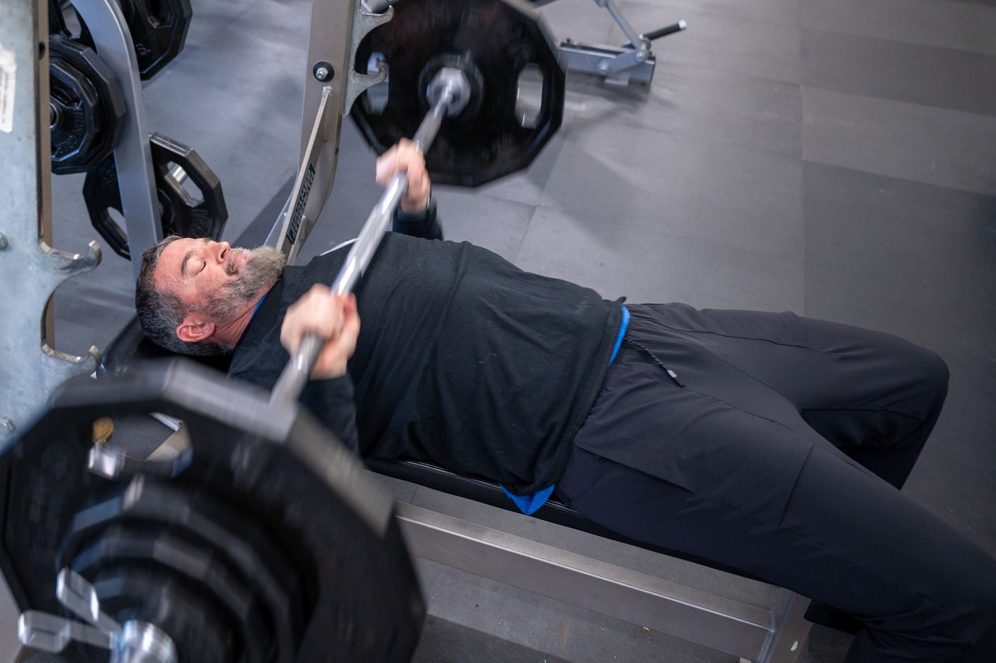 Man bench presses barbell with weight plates. (U.S. Air Force Photo by Airman 1st Class Donnell Ramsey)