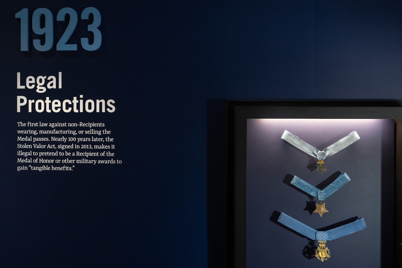 Three medals on ribbons sit in a display case on a wall with writing on it.