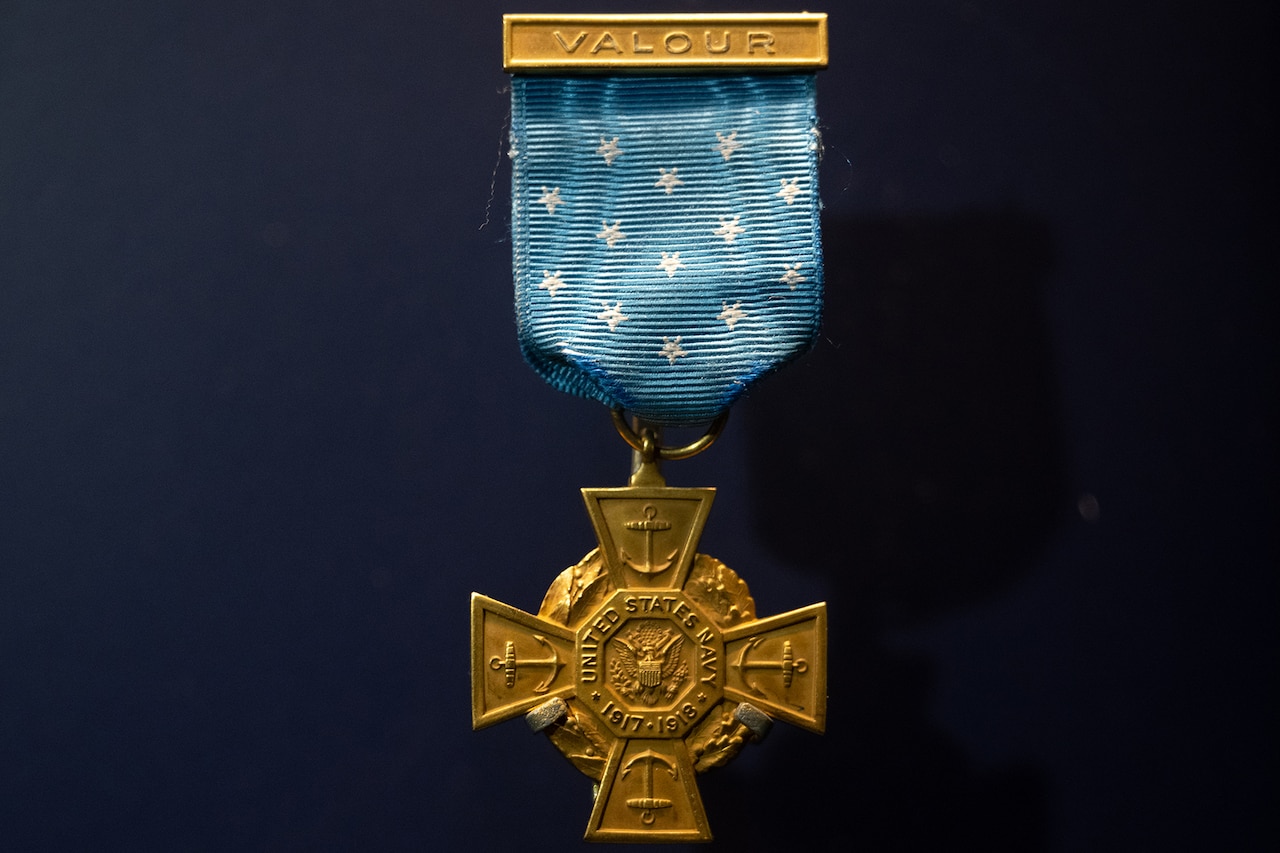 A bronze medal cross hangs off a blue ribbon.
