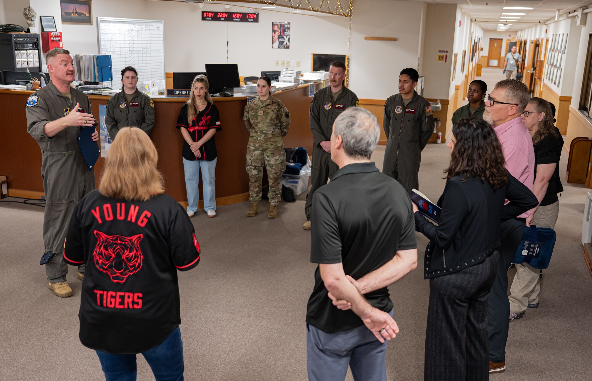 A male Airman gives a briefing to 11 other people standing in a circle.