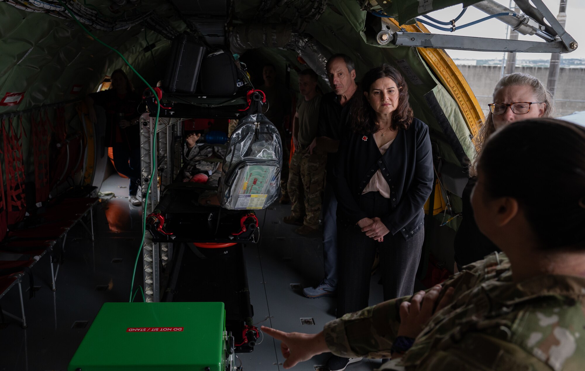 In the foreground a female Airman in uniform points to a green box on the floor of a KC-135 Stratotanker, while other people listen to her explain the purpose for the equipment.