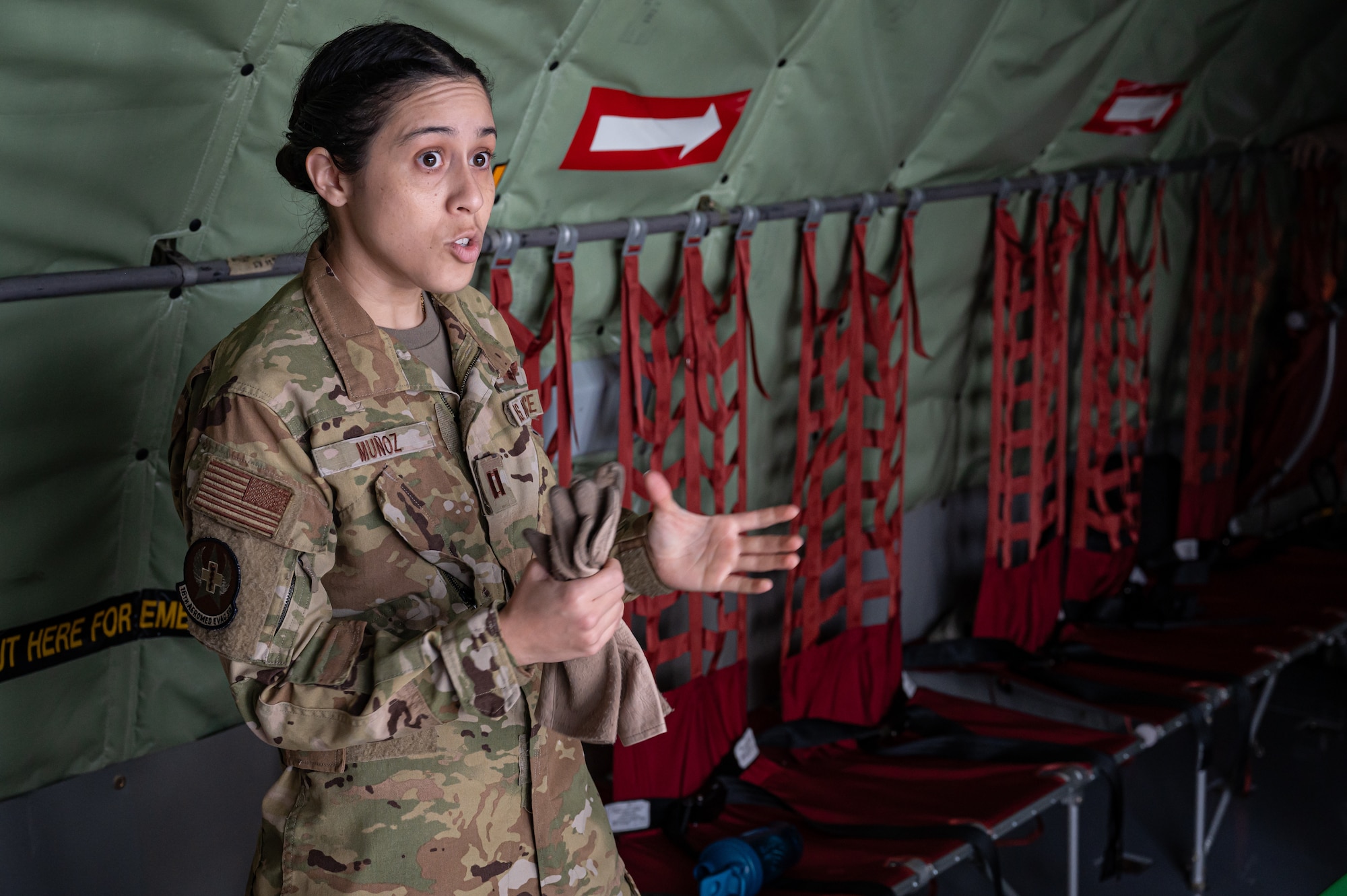 A female Airman talks to a group of people (not shown) in a KC-135 Stratotanker. In the background are red seats with cargo nets as the backrest.
