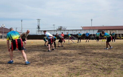 Military members line up on a field during a flag football game.