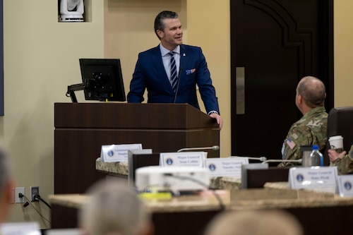 A man in a business suit stands behind a podium smiling while looking to his left.