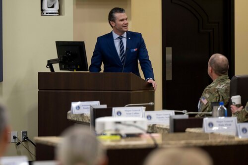 A man in a business suit stands behind a podium smiling while looking to his left.