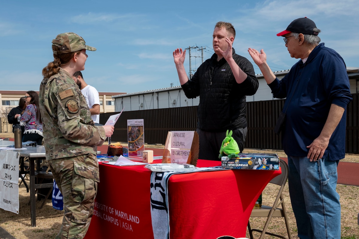 A military member speaks to two civilians during a job fair.
