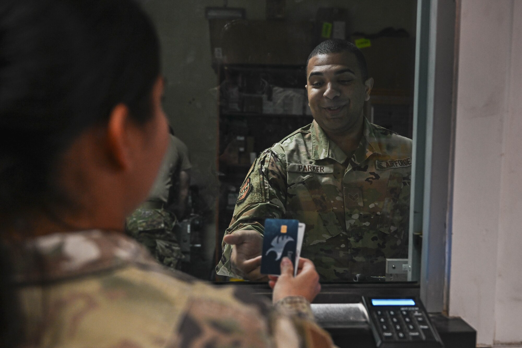 A woman in uniform hands banking cards to a man in uniform behind a pane of glass.