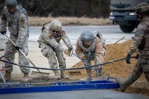 U.S. Air Force and French army members smooth concrete.