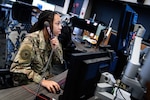 A uniformed military member sits at their computer while answering the phone.