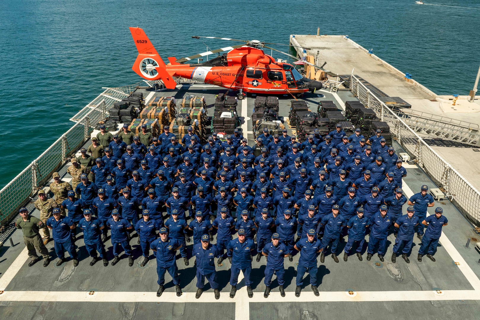 Crew members from USCGC Stone (WMSL-758) stand at parade rest in front of interdicted narcotics at Port Everglades, Florida, Mar. 20, 2025. The Stone's crew secured the illegal drugs from 14 interdictions in the international waters of the Eastern Pacific. (U.S. Coast Guard photo by Petty Officer 2nd Class Taylor Bacon)