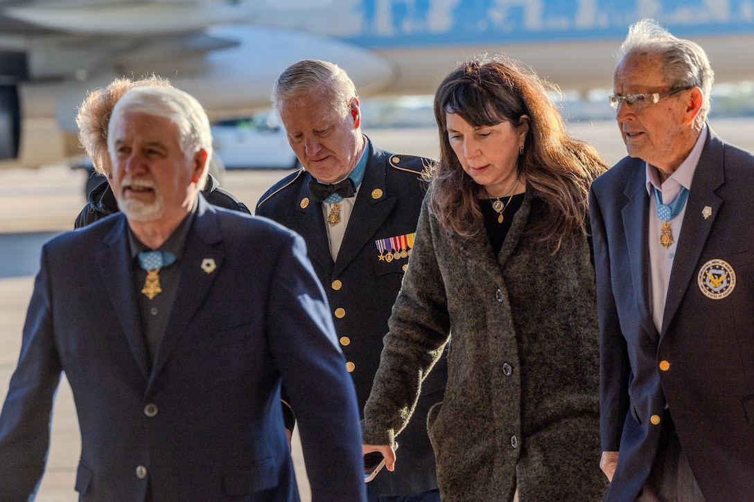 A group of people walk away from a plane in the background on a sunny day.
