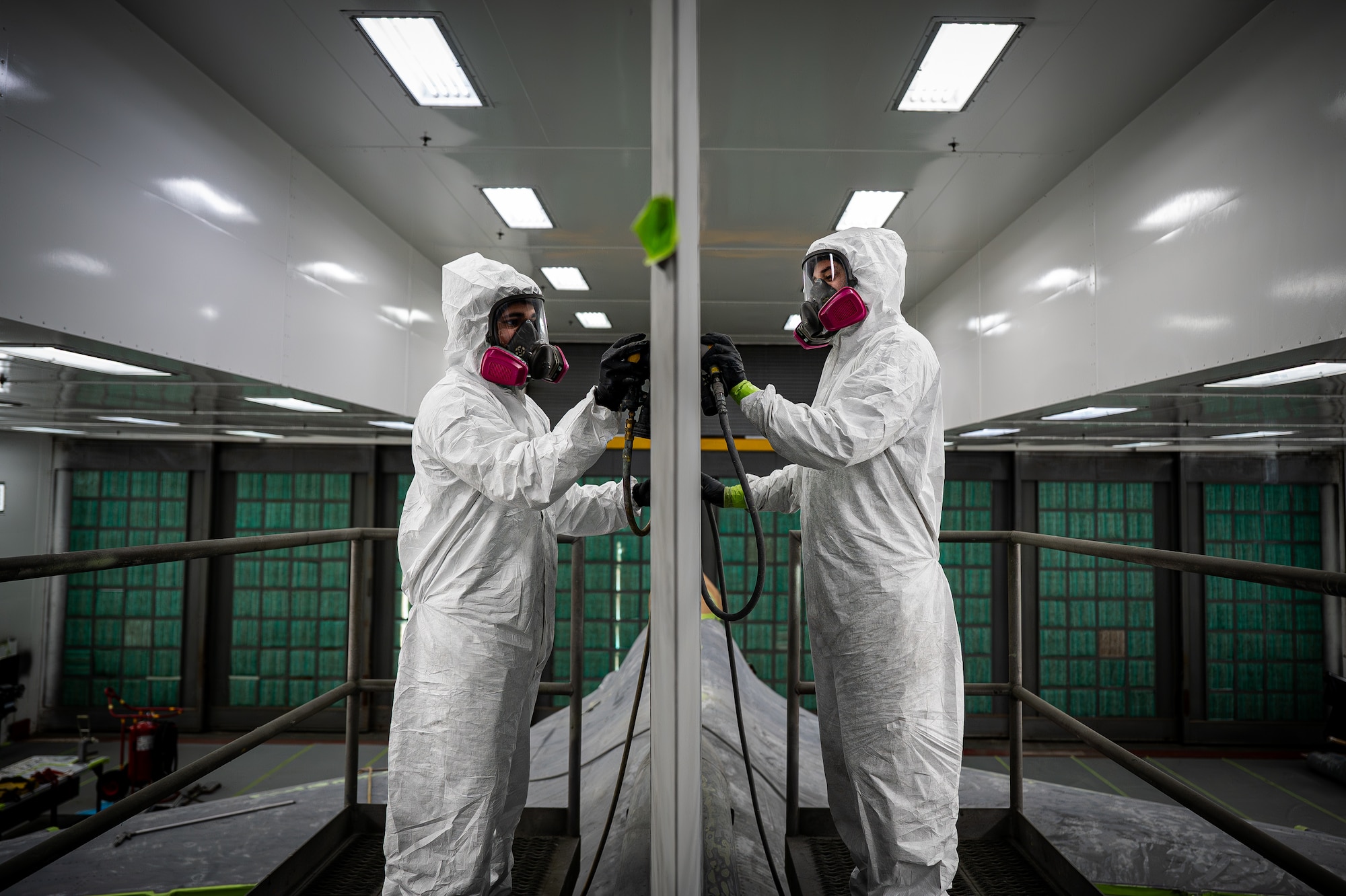 Two people wearing paint equipment paint a jet.