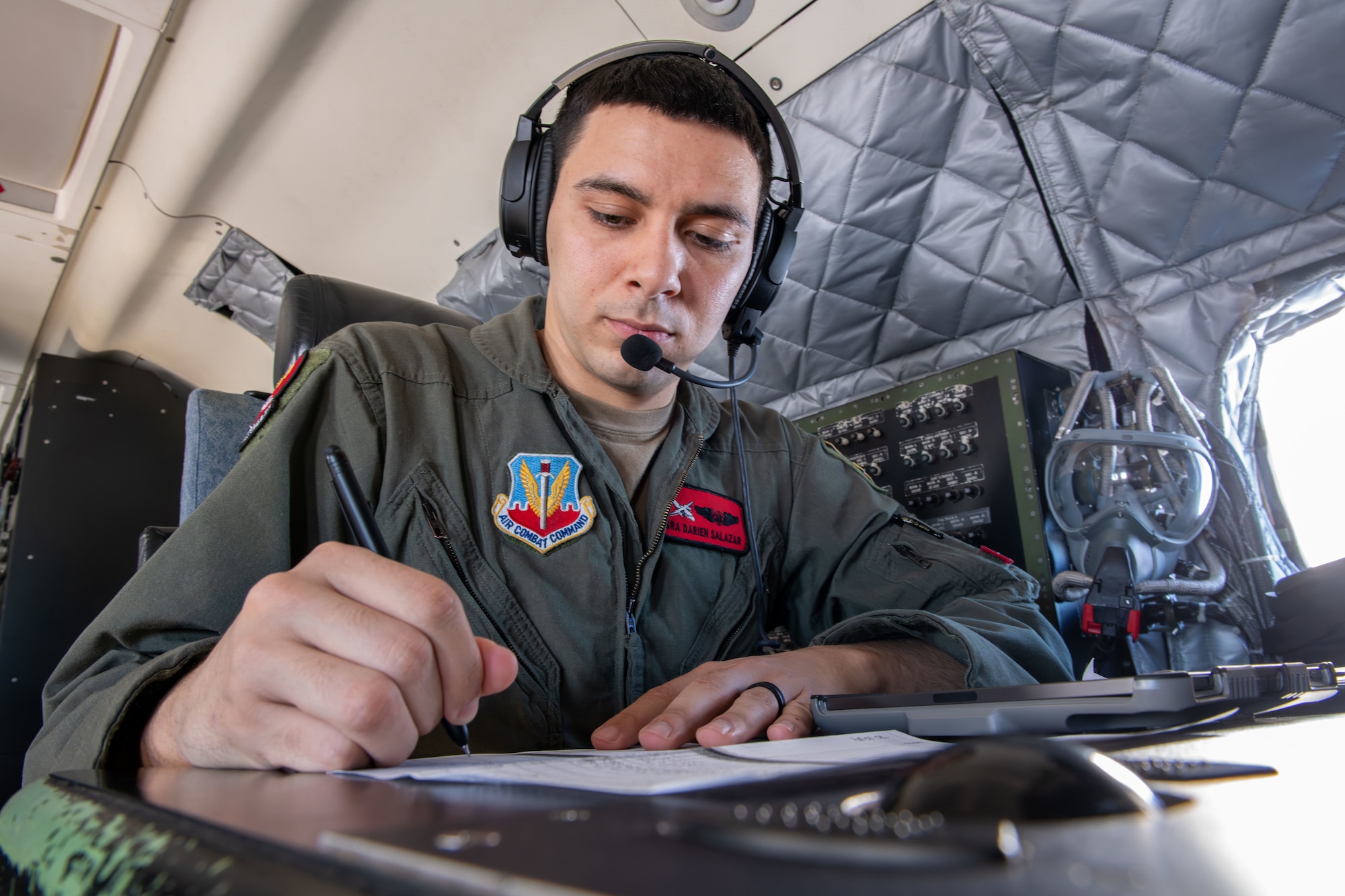 A man is writing on paper with a headset on.