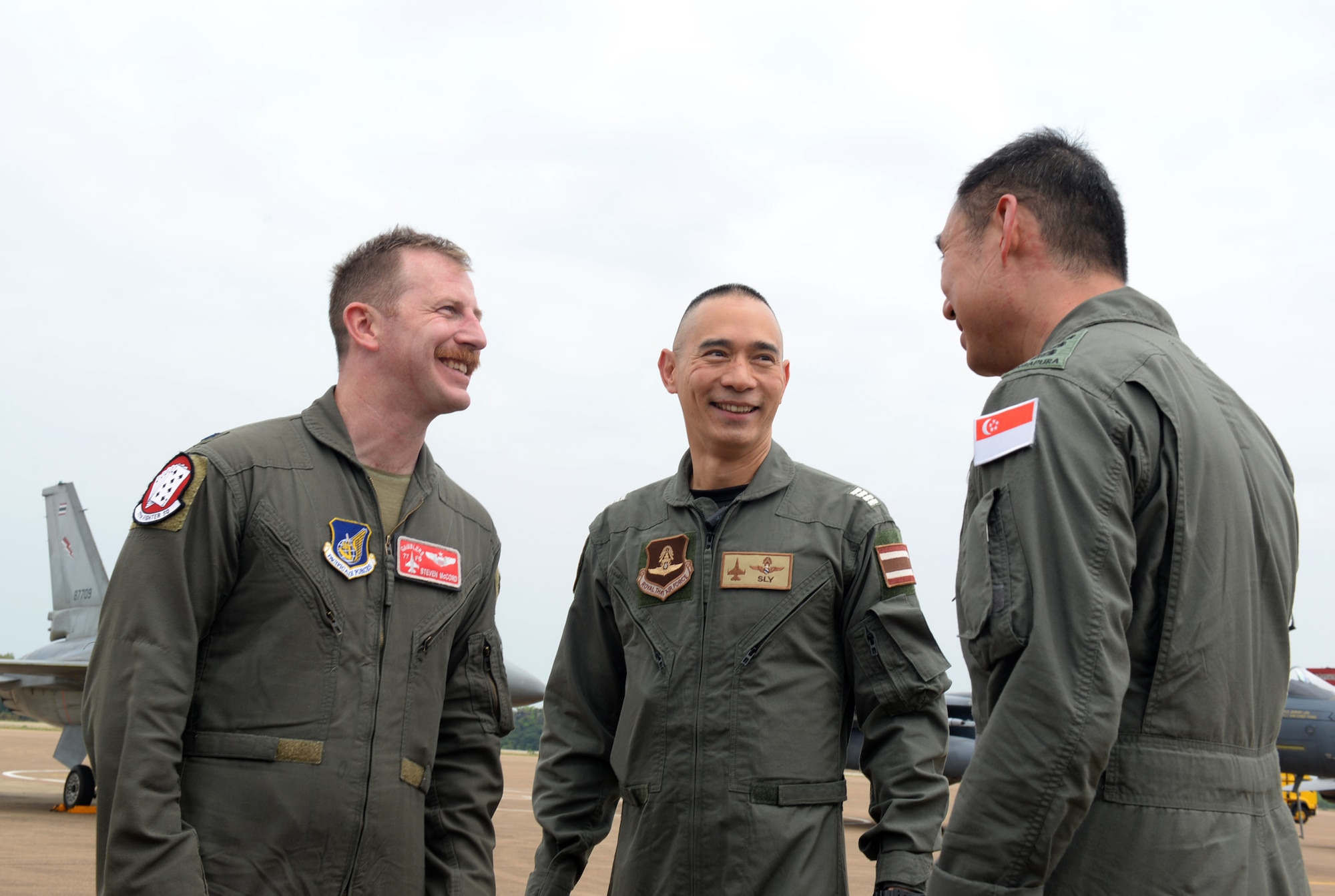 three pilots in jumpsuits smile at each other