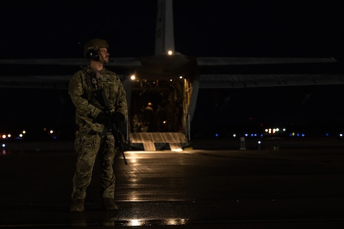 A defender stands guard behind a C-130J Super Hercules.
