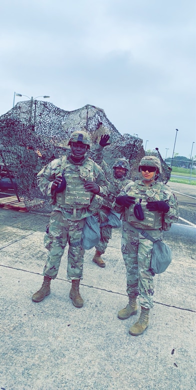 Three U.S. Army Soldier pose together with equipment behind them