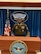 Male U.S. Army Soldier in dress uniform poses behind a Department of Defense podium with the Pentagon logo behind him