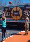 child shooting basketball with service member watching