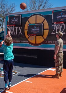 child shooting basketball with service member watching