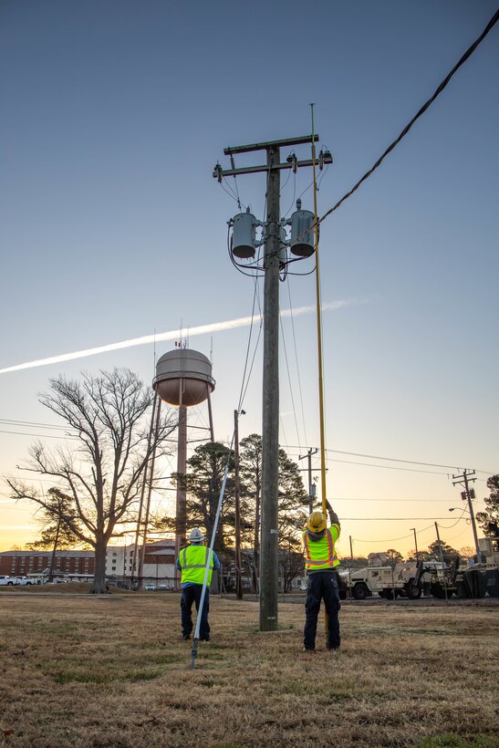 Man in hard hat and protective equipment using a hot stick to close a fuse on an electrical pole.